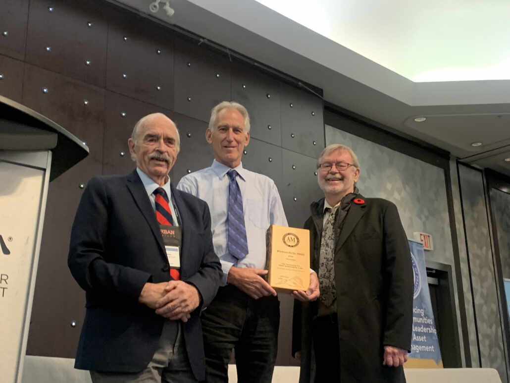 ed Van Der Gulik, President of Partnerships for Water Sustainability in BC, and Kim Stephens, Executive Director at Partnership for Water Sustainability for BC stand together as Wally Wells of Asset Management BC presents them with the 2024 #OurAssetsMatter Award for Asset Management Champion (Organization).